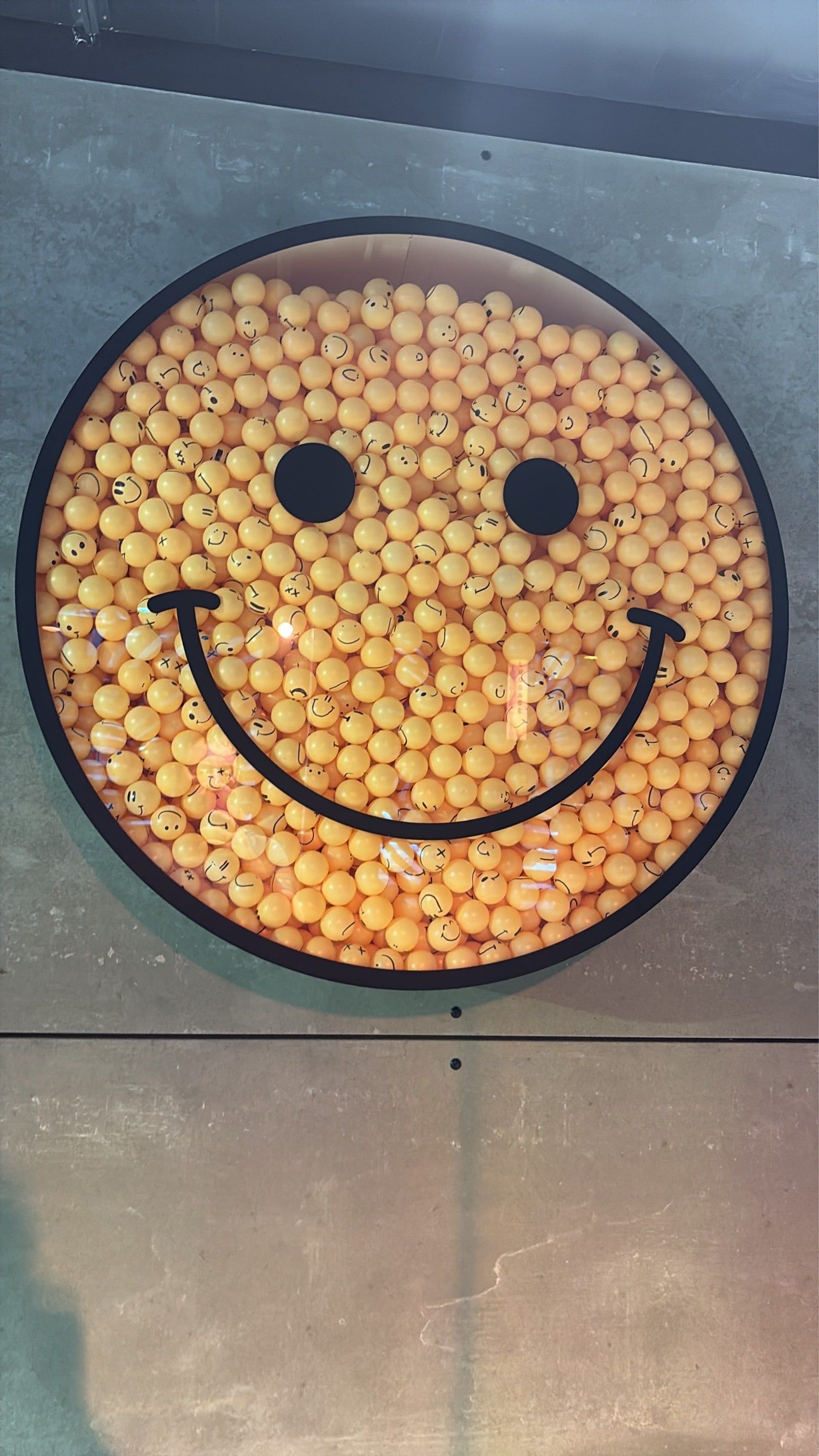 A smiley face container in the wall full of small balls with smiley faces